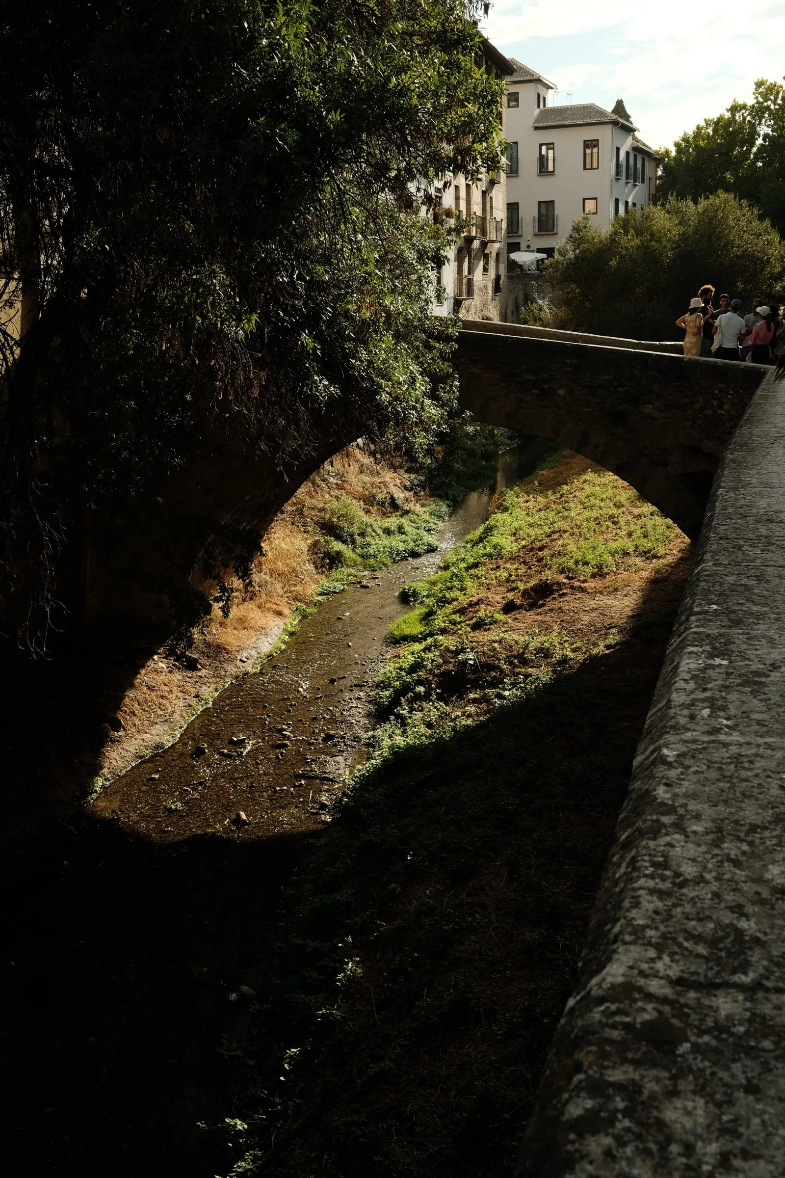 A dark canal between old walls with sunlit buildings above.